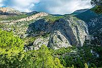 Rocky mountain landscape with steep limestone cliffs, green vegetation and pine forest in the Sierra de Huma near Caminito del Rey, Malaga, Andalusia, Spain under partly cloudy daylight [IBR125527074]