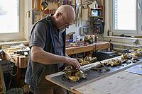 Antique shriner works on parts of a damaged golden baroque frame on the workbench. Russikon, Switzerland [IBR125527113]