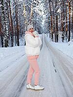 A young girl on the road in a winter forest. Beautiful winter forest with a road. Travel in winter. [IBR125536400]