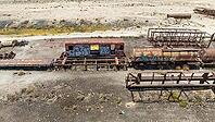 Train Cemetery featuring rusted locomotive skeletons and abandoned railway carriages scattered across the arid desert landscape. Aerial view [IBR125536413]