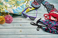 Swimwear, sunglasses, flip flops and beach towel with a tropical print on a wooden table [IBR125536420]