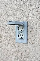 Electric outdoor outlet with lid in a beige stucco wall [IBR125536439]