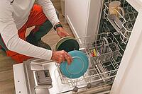Man in a white t-shirt, the dishes in the dishwasher, in the kitchen of his house [IBR125536454]