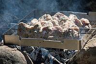 Marinated pork skewers sizzling over hot charcoal with rising smoke seasoned with herbs and spices on metal tray. Outdoor barbecue scene ideal for summer picnics, campfire cooking and appetizing meals [IBR125536458]