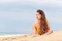 Beautiful woman with perfect body lies on sandy beach, wearing yellow bikini, sunbathing at beach resort, enjoying summer vacation [IBR125536482]