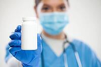 Women UK NHS general professional doctor, laundry, protective face mask and gloves, holding white empty bottle pills, blank no label container suitable for adding custom text, selective focus [IBR125557531]