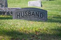 Antique grave stone reads husband in tranquil green grass cemetery with sunshine and dappled sunlight. Large letters are readable. No people with copy space [IBR125557562]