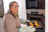 Elderly white-haired woman putting a tray of cookies into the ovens [IBR125557576]