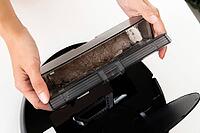 Robot vacuum cleaner in female hands. Woman takes out container and filter to clean it from dirt and debris. Concept of cleaning with cordless vacuum cleaner, close-up [IBR125557579]