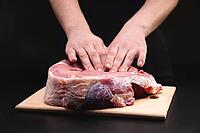A man massages a fresh piece of beef with his hands on a wooden cutting board. Close up on black background [IBR125557615]