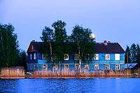 The full-orbed moon rises over the spring river, forest and village during the daytime, quiet evening romantic nature. Two-storey old wooden house on the river bank [IBR125565994]