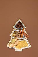 Cloves, cinnamon, nutmeg, cardamom and ginger for making ginger cookies in a box in the shape of a Christmas tree on a brown background with copy space. Concept of festive Christmas baking. Top view, flat lay [IBR125566003]