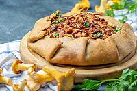 Homemade pie with wild chanterelles, onion, potatoes and greenery on a textured dark background, selective focus [IBR125566009]