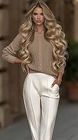 A poised blonde woman with long wavy hair wears a beige knit sweater and white pleated trousers on a softly blurred urban city street. AI generated [IBR125592654]