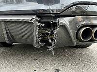 Fractured composite panels hang beneath the rear bumper, revealing wiring and underbody parts beside metal exhaust outlets above the pavement, AI generated [IBR125592656]