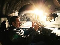 A man's startled face and raised hands fill the foreground, while a steel truss bridge and intense sunlight appear beyond the windshield, AI generated [IBR125592659]