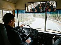 A wide mirror reflects rows of children seated behind the driver as the bus follows a curving woodland road, with the dashboard and phone in view, AI generated [IBR125592662]
