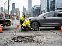 Traffic cones mark the work area as a flatbed tow truck waits nearby, while modern office towers rise above cracked pavement in daylight, AI generated [IBR125592665]