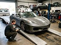 A second sedan sits elevated on a hydraulic lift as tools, tires, metal ramps and workshop equipment fill the indoor service bay, with storage shelves, AI generated [IBR125592669]