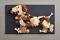 Cheese, cured meats, crackers and rosemary are arranged in a playful dog shape on a dark slate charcuterie serving board. AI generated [IBR125592674]