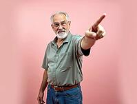 Cheerful mature man pointing index finger indicating something interesting on pastel pink background, AI generated [IBR125592675]