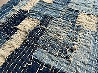 Layered cotton patches, frayed edges, and irregular hand stitching reveal the coarse weave of a timeworn blue-and-cream textile in close detail, AI generated [IBR125592683]