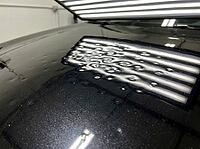 Black car hood displays multiple dents from hail, clearly visible under professional light bars, indicating severe damage needing expert paintless dent repair and auto body restoration, AI generated [IBR125592697]