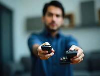 Man fighting to operate television, holding multiple remote controls with a confused expression, AI generated [IBR125592699]
