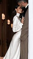 A woman in a flowing white satin gown leans seductively into a suited man in a warmly lit, elegant interior. AI generated [IBR125592702]