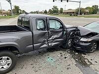 Broken glass, debris, and dark fluid cover the pavement beneath deployed airbags, as damaged vehicles block part of a signalized intersection, AI generated [IBR125592707]