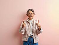 Smiling senior woman showing thumbs up gesture, expressing positivity and approach on pink background, AI generated [IBR125592719]