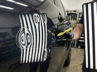 A gloved hand uses a yellow marker beside reflected inspection lines to locate panel damage in a professional auto body repair workshop setting, AI generated [IBR125592721]
