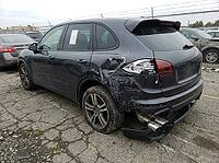 Parked among other vehicles on cracked pavement, the dark crossover shows torn bodywork, a damaged rear bumper, exposed exhaust tips, and a window tag, AI generated [IBR125592723]