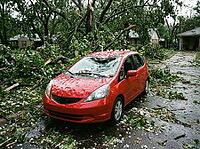 Hailstones cover the wet pavement and car while snapped tree limbs, broken branches, and debris fill a residential driveway after severe storm damage, AI generated [IBR125592731]