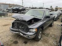 Gray pickup truck displaying severe front end damage from a collision, parked in an outdoor salvage yard surrounded by other derelict vehicles awaiting dismantling and recycling, AI generated [IBR125592733]