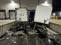 At a brightly lit freight facility, a detached box trailer leans beside a tractor while broken parts and dark fluid cover the concrete, AI generated [IBR125592736]