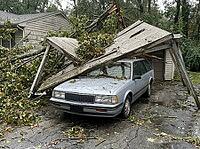 Broken branches and roofing panels cover the driveway around the vehicle, while a house and dense trees frame the residential scene, AI generated [IBR125592746]