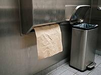 Brown paper towel hangs from a stainless wall dispenser beside an open pedal bin, showing a simple setup for hand drying and waste disposal, AI generated [IBR125592747]