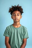 Sad pre-adolescent boy with curly hair posing in a studio with a light blue background, AI generated [IBR125621278]