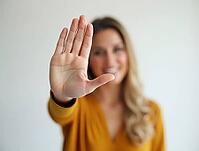 Smiling woman showing stop gesture with hand in bright studio setting, AI generated [IBR125621287]