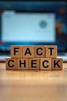Wooden blocks spelling fact check in front of a blurred laptop screen, AI generated [IBR125621307]