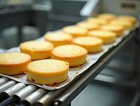 Freshly baked round sponge cakes moving along an assembly line, illustrating the production process in a food processing plant, AI generated [IBR125621347]