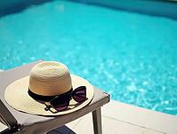 Straw hat and sunglasses are placed on a deck chair near a beautiful blue swimming pool, embodying the essence of summer relaxation and vacation bliss, AI generated [IBR125636897]