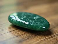 Polished green gua sha stone sits on wooden table, promoting wellness, self-care, and relaxation, AI generated [IBR125636899]