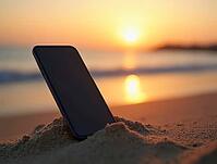 Mobile phone standing in the sand with ocean waves and sunset bokeh in the background, AI generated [IBR125636920]