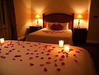 Rose petals scattered on bed surface in romantic honeymoon suite illuminated by warm candlelight, AI generated [IBR125636922]