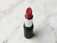 Red lipstick in black and silver tube standing on a marble surface, beauty product, AI generated [IBR125636929]