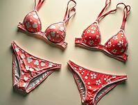 Two matching coral pink bikini sets, one with a flower print and the other with a cloud print, displayed on a beige surface, AI generated [IBR125645940]