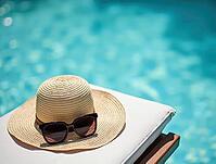 Straw sun hat and sunglasses are resting on a lounge chair beside a sparkling blue swimming pool, inviting relaxation, AI generated [IBR125645949]