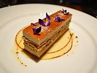 Delicious french mille-feuille dessert served on a white plate, garnished with edible flowers and caramel drizzle, AI generated [IBR125653431]